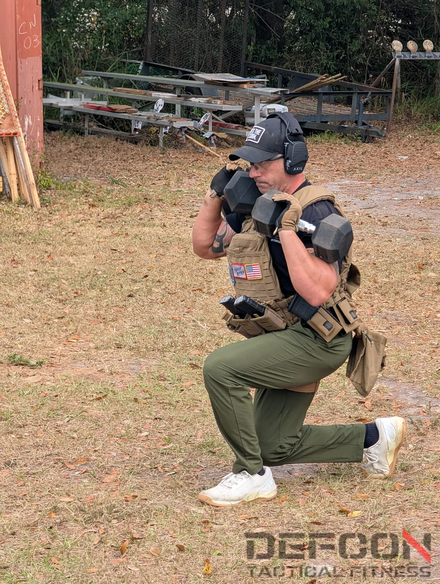 A DEFCON athlete in a plate carrier doing weighted dumbbell lunges at a TACFIT event